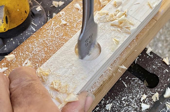 Person uses a spade bit to drill through pine