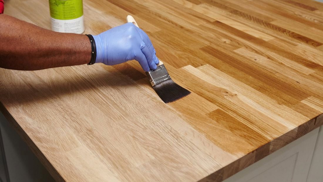 Person using paint brush to apply clear hard wax oil to benchtop.