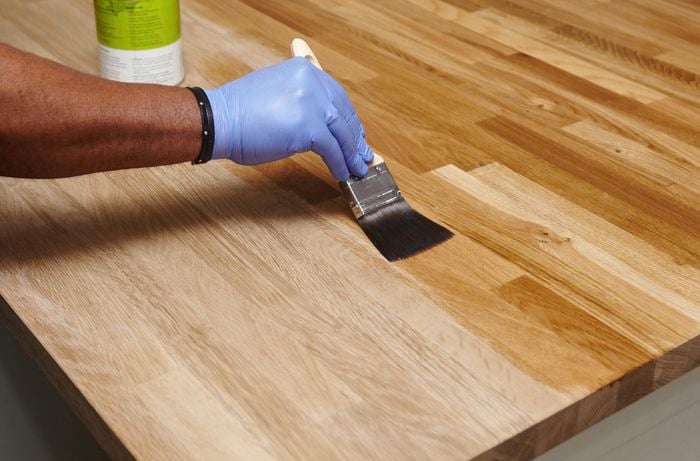 Person using paint brush to apply clear hard wax oil to benchtop.