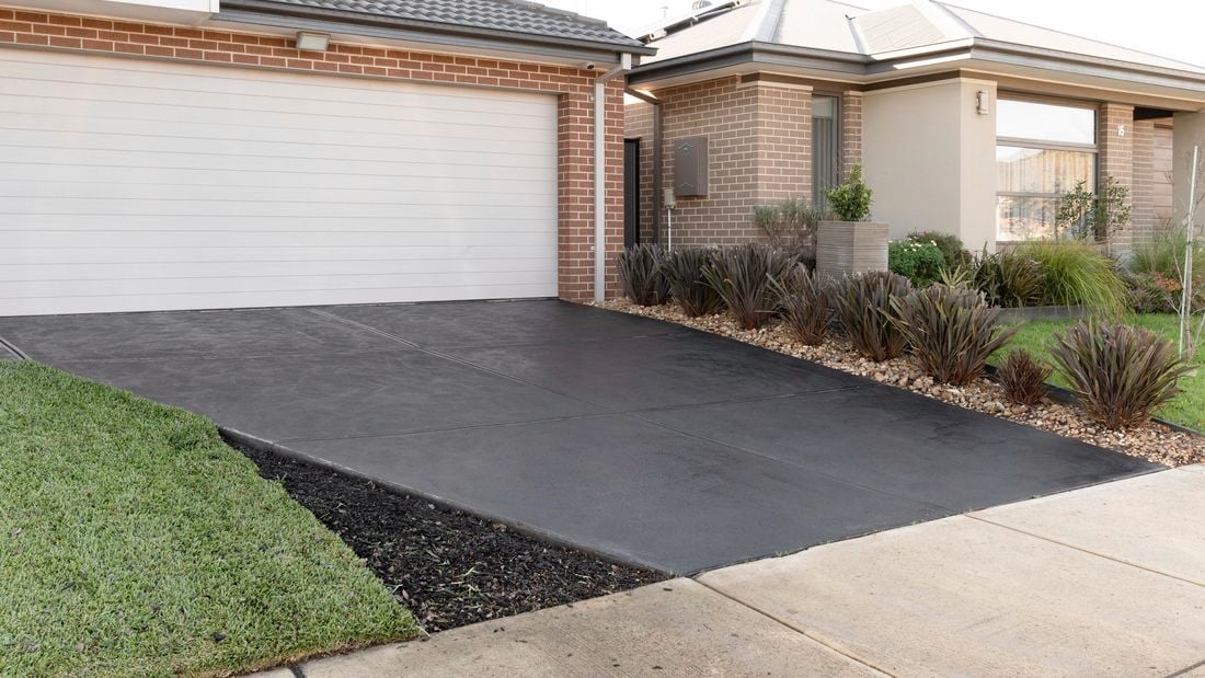 Looking at a new sealed driveway, house has red bricks and shrubs in garden bed