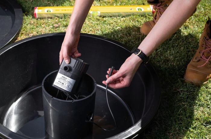 A person placing a pump inside a chamber of a water feature