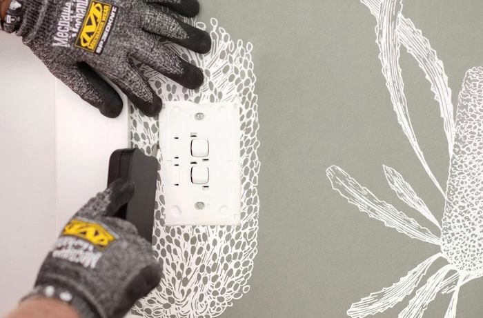 The image displays two hands trimming wallpaper around a hole or powerpoint