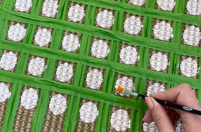 Hand painting green squares and white circles onto brown hessian.