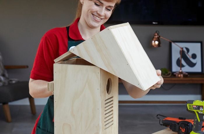 A loop being drilled into a completed bird box with wire to secure it to a tree