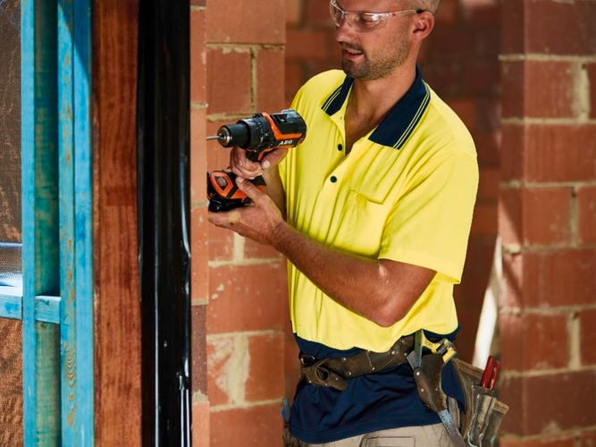 Trqadesperson in a hi vis polo shirt using a drill on house framing