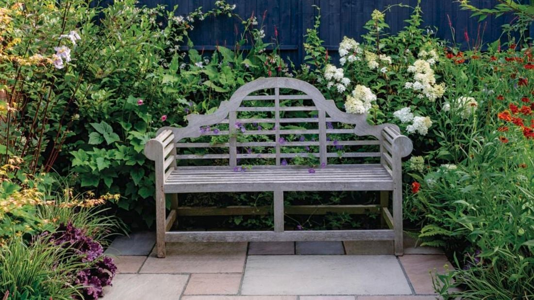 Pathway leads to outdoor bench seat surrounded by a variety of greenery and flowers.