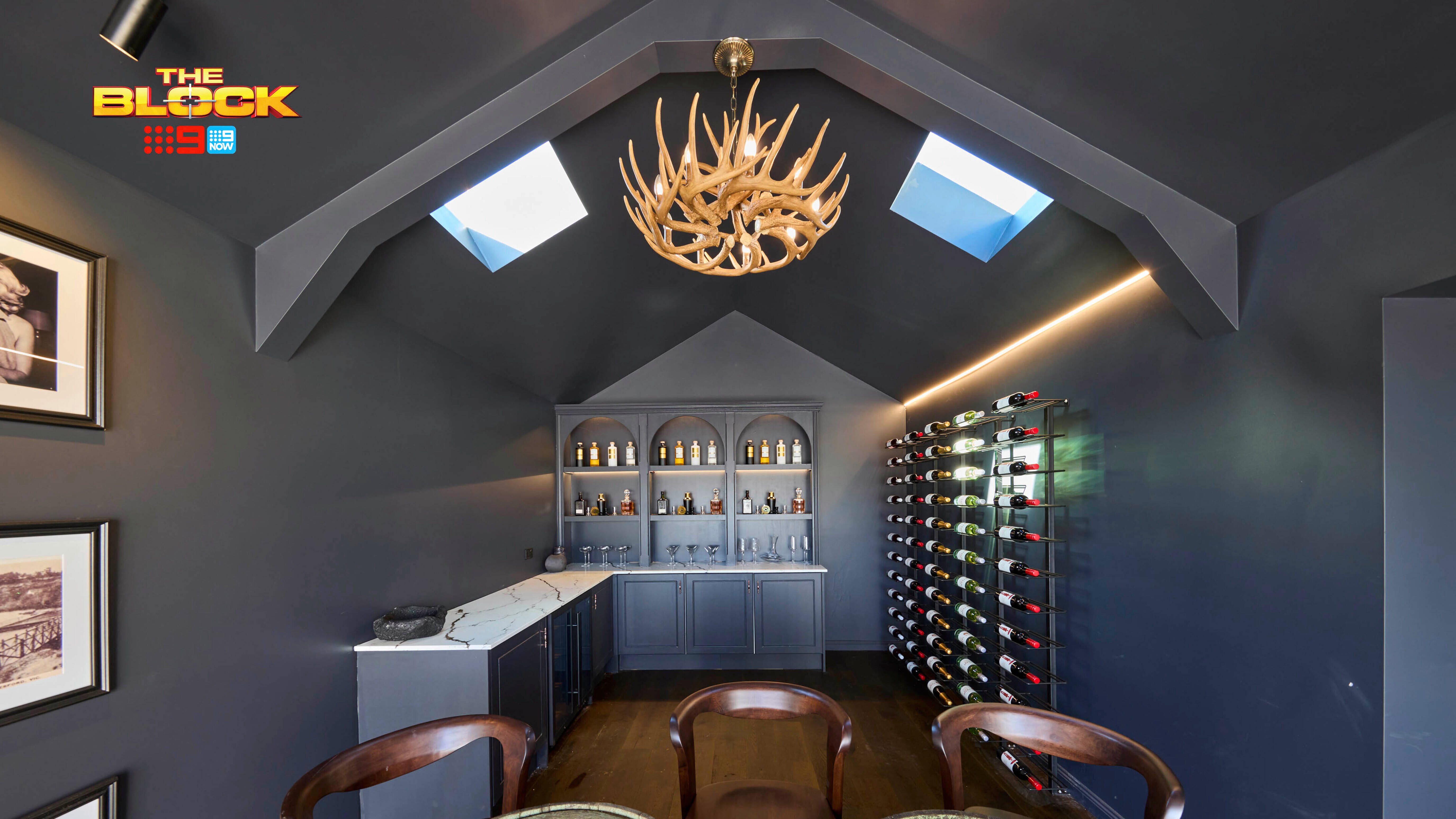 A room with lots of bottles of wine next to a wall, and two table and three chairs in it.