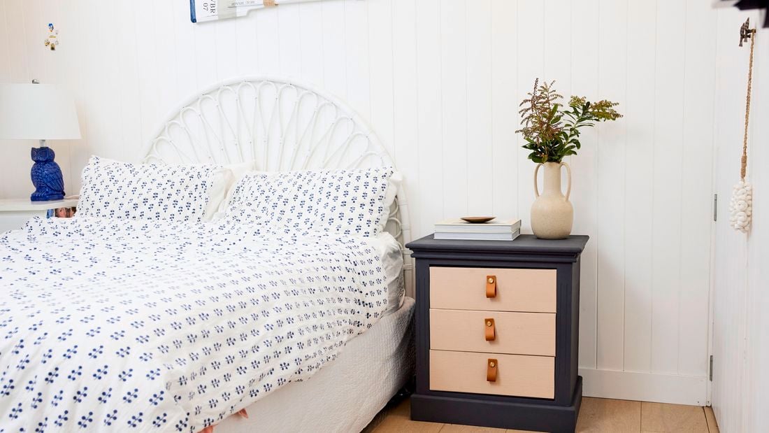 Upcycled bedside table with flower vase on top and next to a bed in the bedroom.