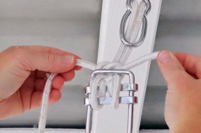 A person ties a knot at the top of brackets to secure cord