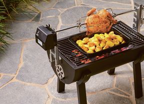 Charcoal chicken and roasted potatoes cooking on a rotisserie grill on a patio.