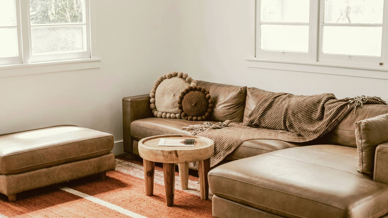 Living room with brown leather sofa, ottoman, wooden side table and orange striped rug.