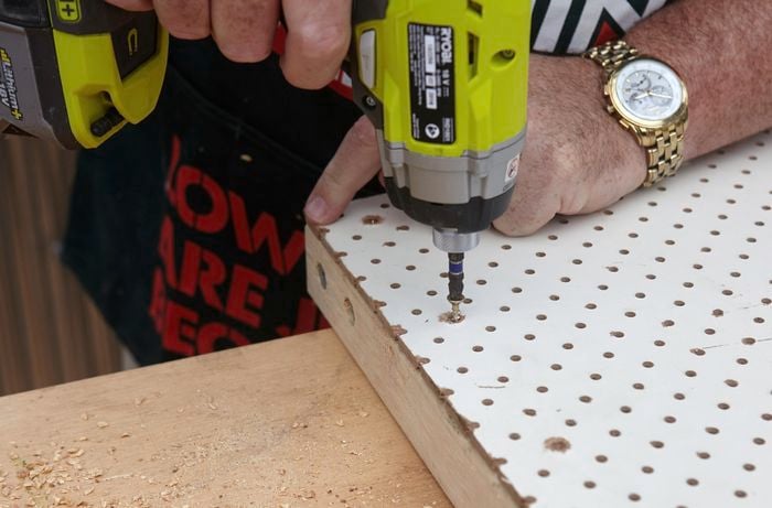 A person attaching pegboard to a pine frame using a cordless driver