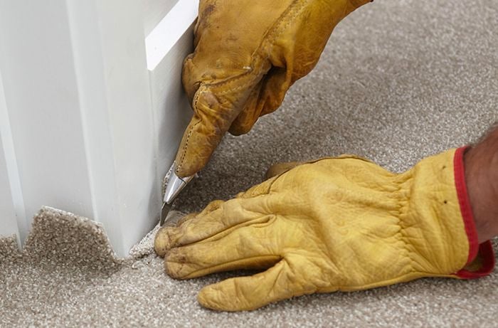Excess carpet being trimmed from the moulding of a wall
