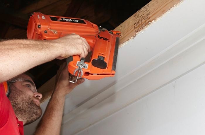 A person using a nail gun to attach a noggin around a hole in a ceiling