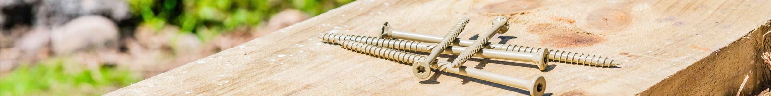 Several screws placed on a wooden plank outdoors.