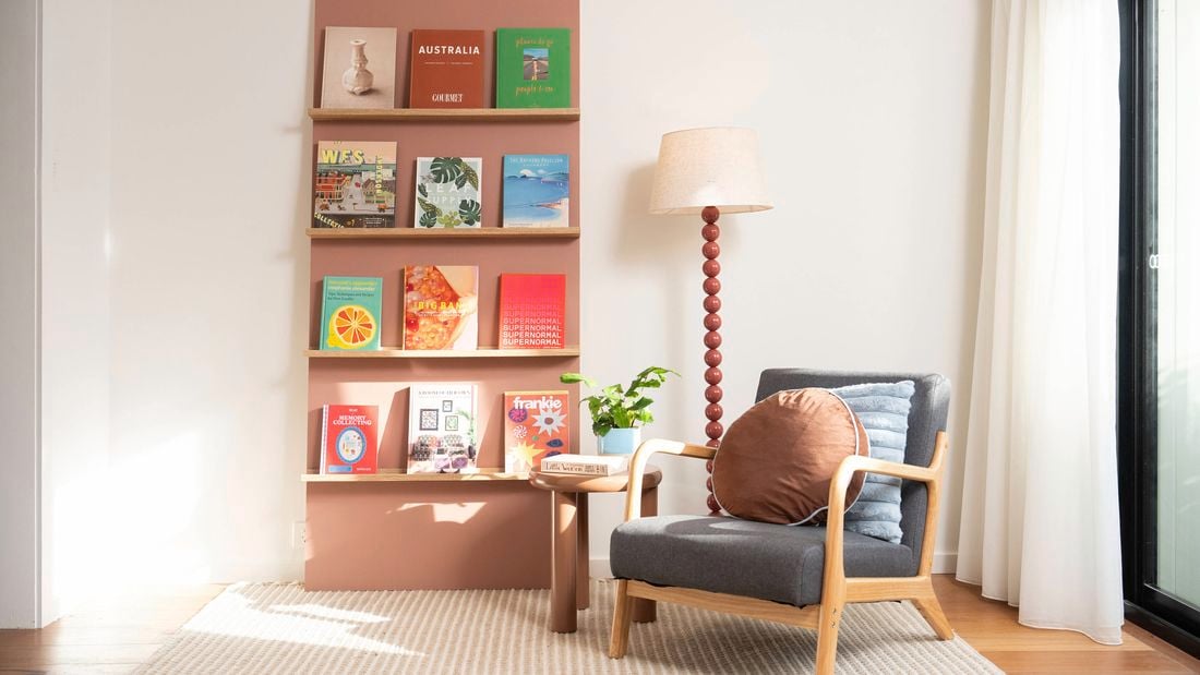 DIY bookshelf made from painted wall panels with timber ledges, styled with books, a floor lamp and armchair.