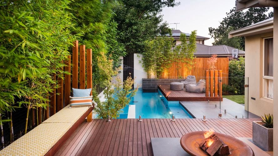 An outdoor entertaining space with pool, glass fence panels, decking and fire pit.