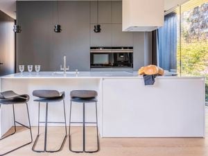 A modern kitchen with a bread on the benchtop, stools, and grey cabinets
