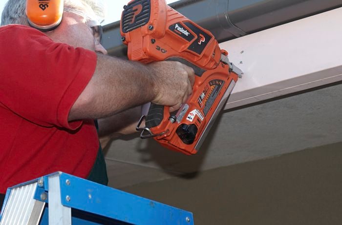 Person nailing pergola frame to roof.