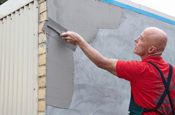 A Bunnings team member applying render to a concrete wall with a trowel