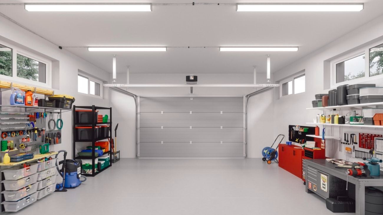 A large, bright garage with a grey car door and flooring. Storage shelves and units line the walls