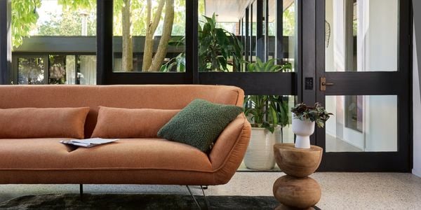 Burnt orange lounge, timber side table all sitting on a thick charcoal rug in living room.
