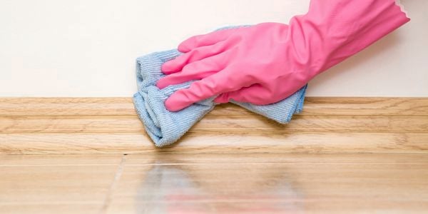 Gloved hand using a micro-fibre cloth to wipe skirting boards.