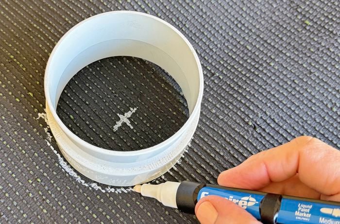 A hand holding a white marker draws around a 90mm circle pipe on the back of a turf mat