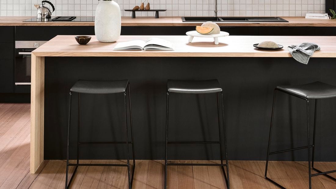 A simple kitchen with black cabinetry, wooden floors and countertops, and white tiled splashback