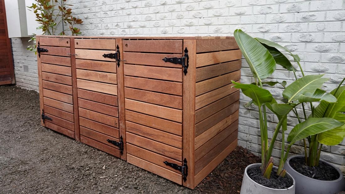 Bin storage unit made of timber, with plants beside.