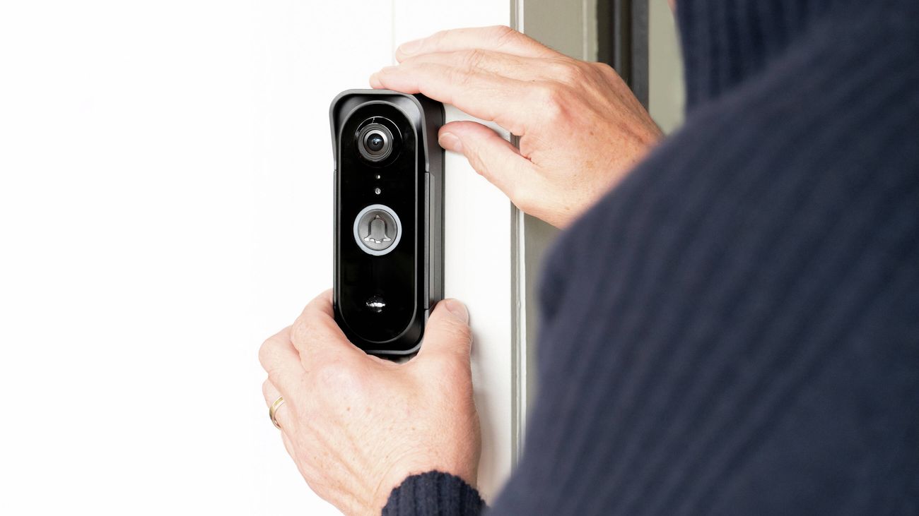 Person installing a smart video doorbell on a door frame.