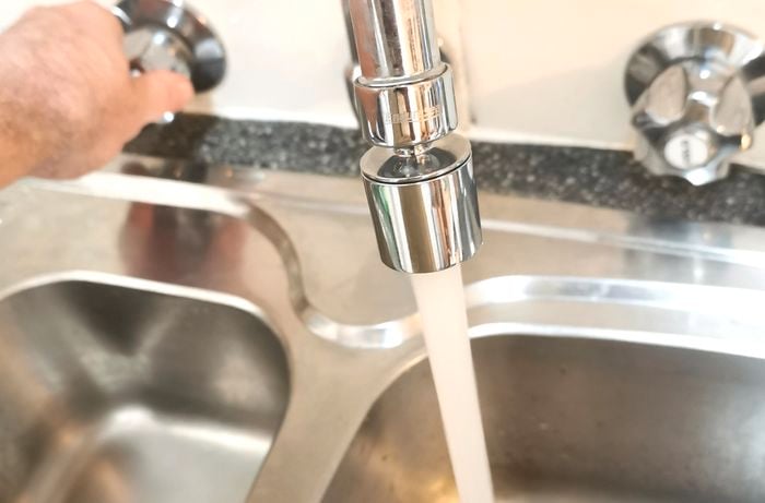A hand turning a tap on. Clean flowing water is coming out of the tap.