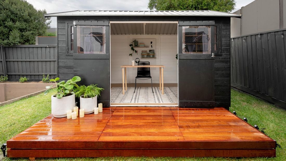 A finished backyard shed, painted black and with a wooden stained deck