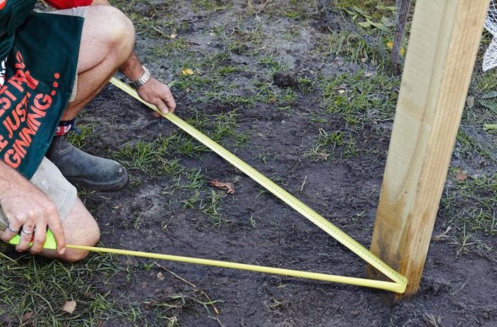 Person using measuring tape around a piece of timber that's stuck into the ground.