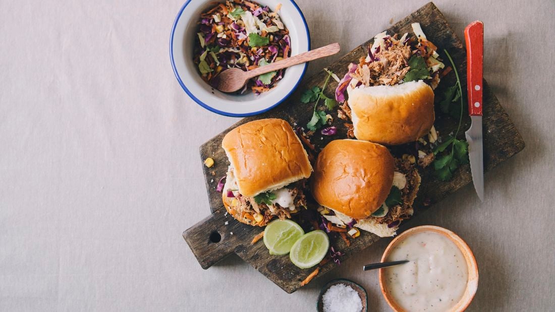 Burger rolls filled with pulled pork on a serving board with side salad