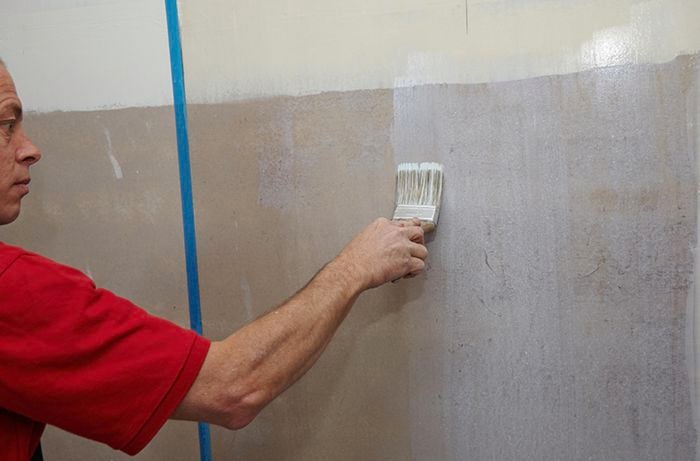 A person painting primer onto a bathroom wall