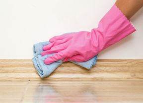 Gloved hand using a micro-fibre cloth to wipe skirting boards.