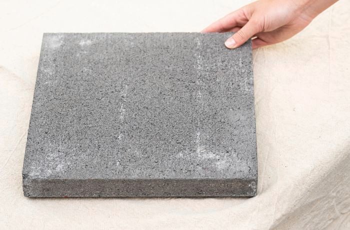 A concrete paver tile is placed on a drop sheet to prepare for a reusable hopscotch path.