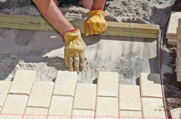 A person removing some sand by hand in front of newly laid pavers