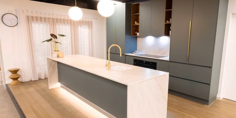 A modern green kitchen with a marble white benchtop and wooden floorboards.