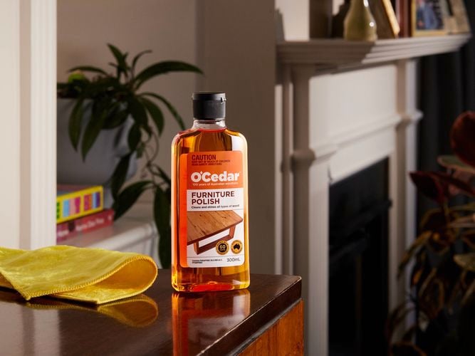 A bottle of O'Cedar Furniture Polish on a wooden Buffet.