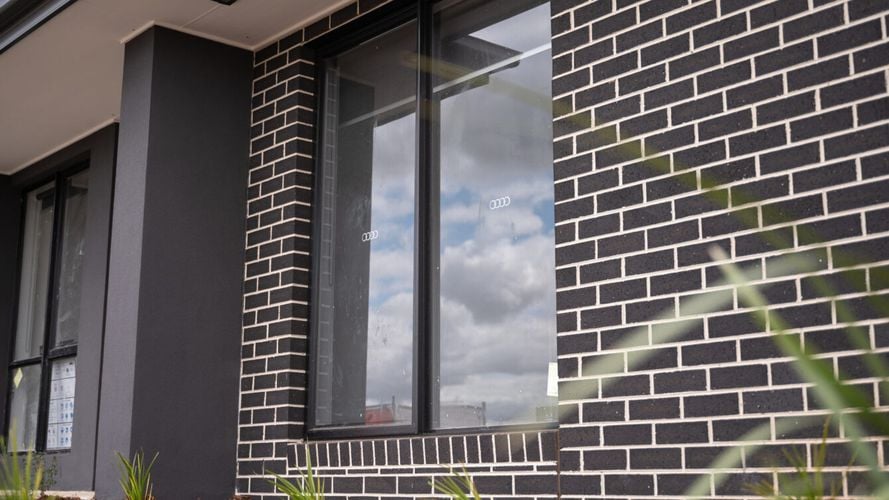 Black brick house wall with large window and garden bed