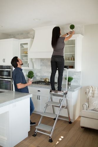 Woman standing on ladder decorating kitchen with indoor plants