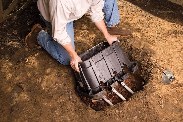 Person placing a sprinkler control valve box into a hole in the ground