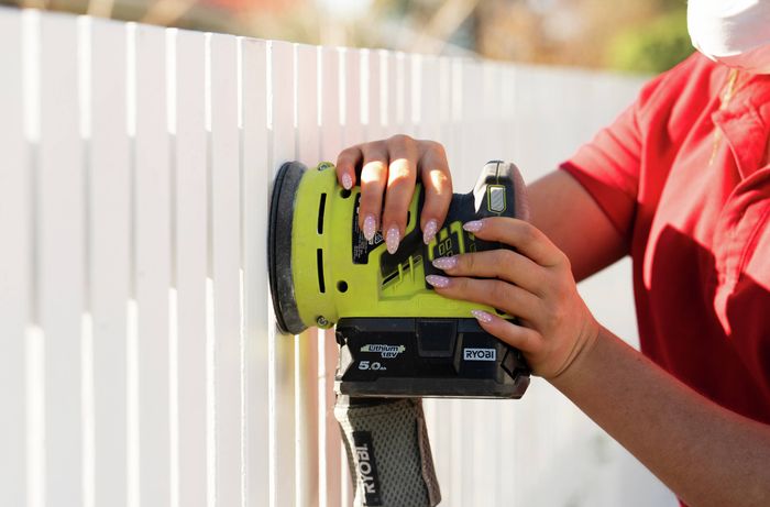 Preparing a picket fence with a power sander before spray painting​​​ 