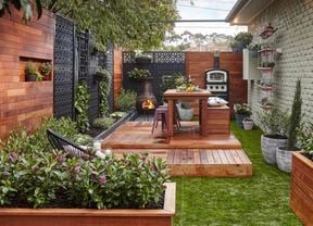 Raised deck with table setting amid a grassed area fenced by timber panels