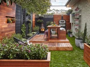 Raised deck with table setting amid a grassed area fenced by timber panels