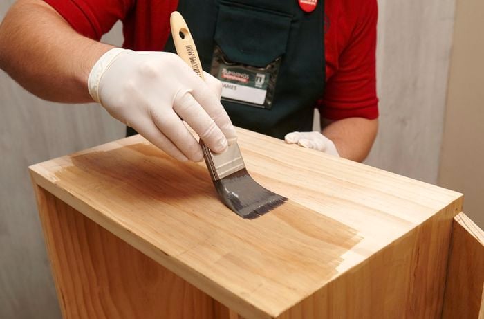 Person painting timber with paint brush and varnish.