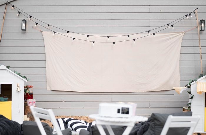 Outdoor table and chairs in front of a wall with canvas screen and fairy lights