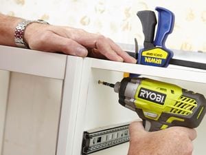 Person attaching two kitchen cabinets using a clamp and cordless driver